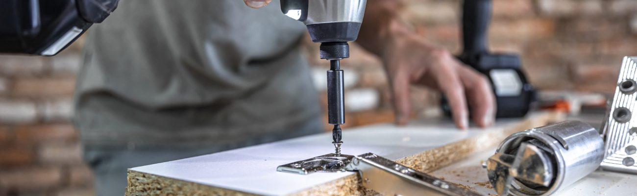 Screwing a self-tapping screw into a metal fastening hole on a wood strip using a screwdriver, the work of a carpenter.