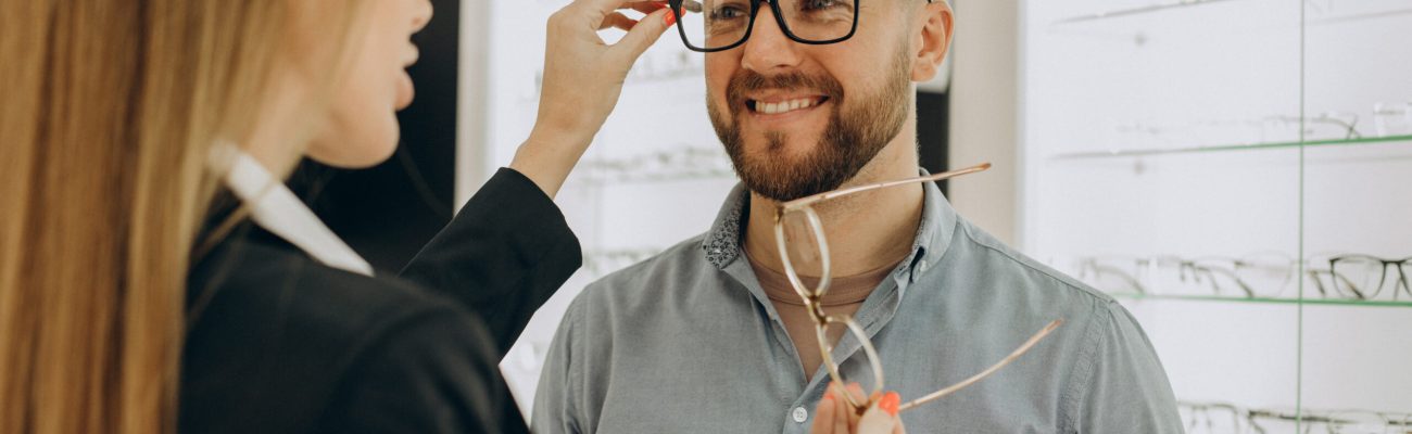 Customer shoosing spectacles at optic store with the lelp of sales person